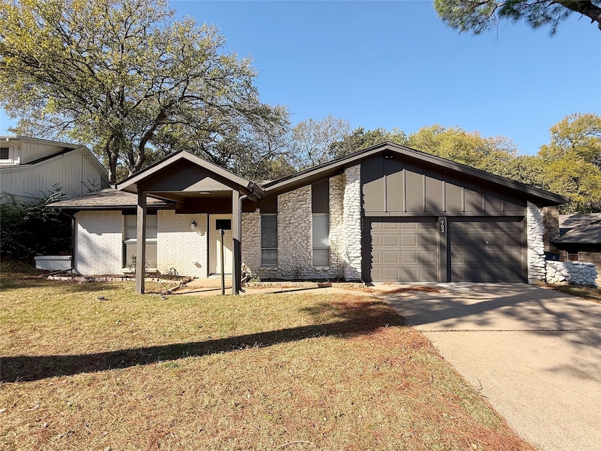 Mid-century home featuring concrete driveway, stone siding, a front yard, an attached garage, and board and batten siding