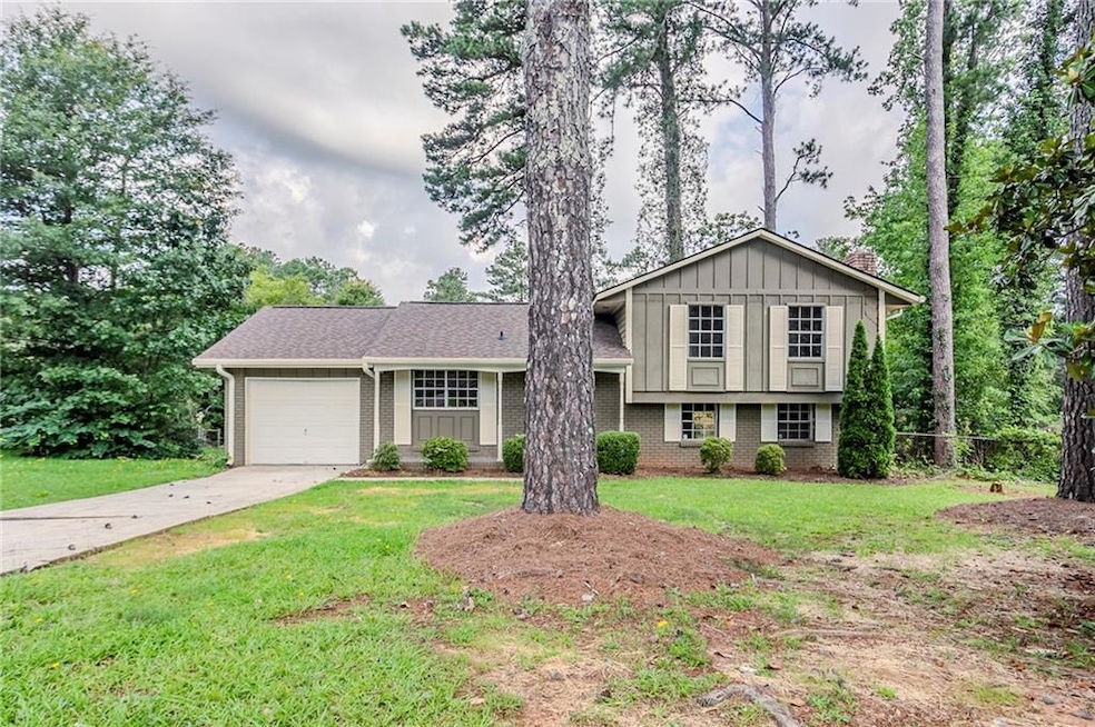 Split level home with brick siding, an attached garage, concrete driveway, a chimney, and a front yard