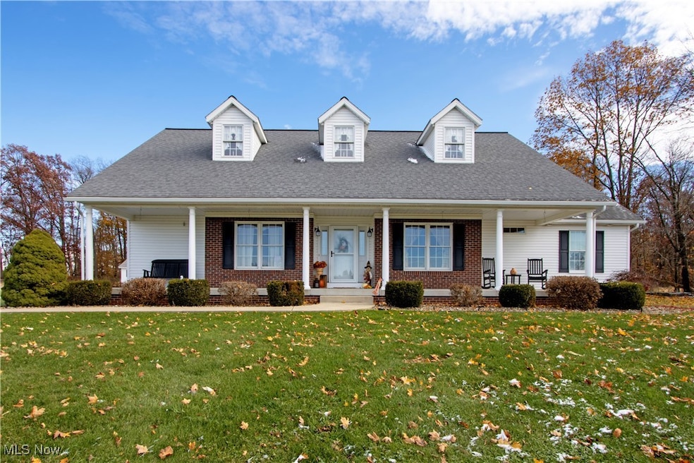 Cape cod-style house with a front yard, covered porch, a shingled roof, and brick siding