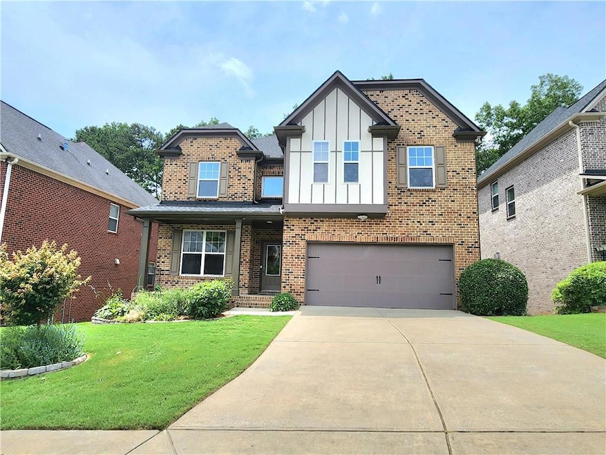 View of front of home with board and batten siding, an attached garage, concrete driveway, a front lawn, and brick siding