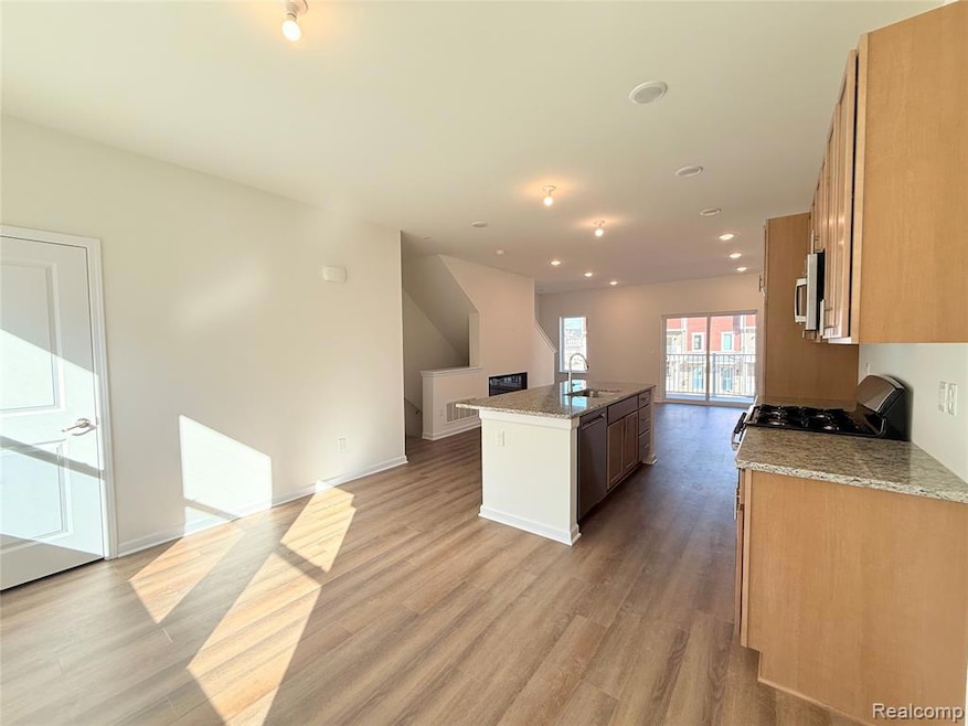 Kitchen featuring light stone counters, a kitchen island with sink, recessed lighting, appliances with stainless steel finishes, and light wood-type flooring