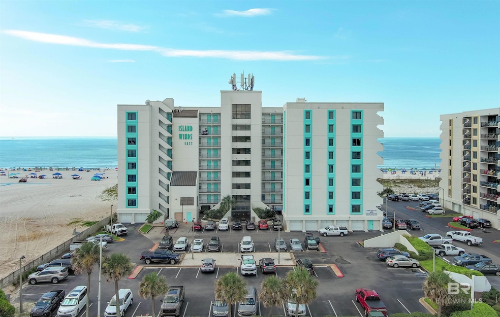 View of apartment building / complex featuring view of water and beach and uncovered parking