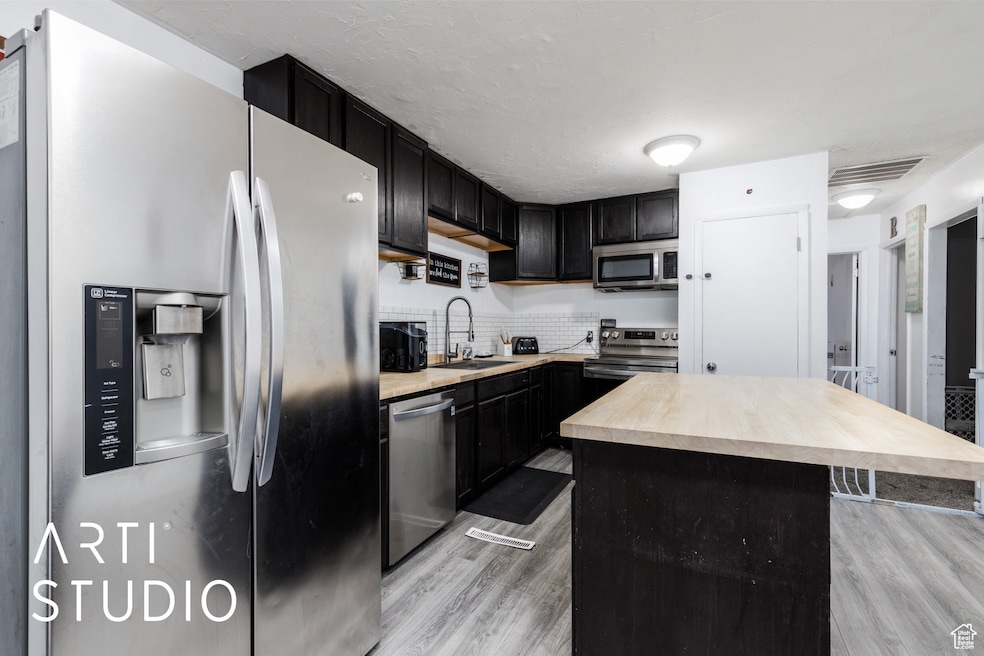 Kitchen with stainless steel appliances, light wood finished floors, dark cabinets, decorative backsplash, and a kitchen island