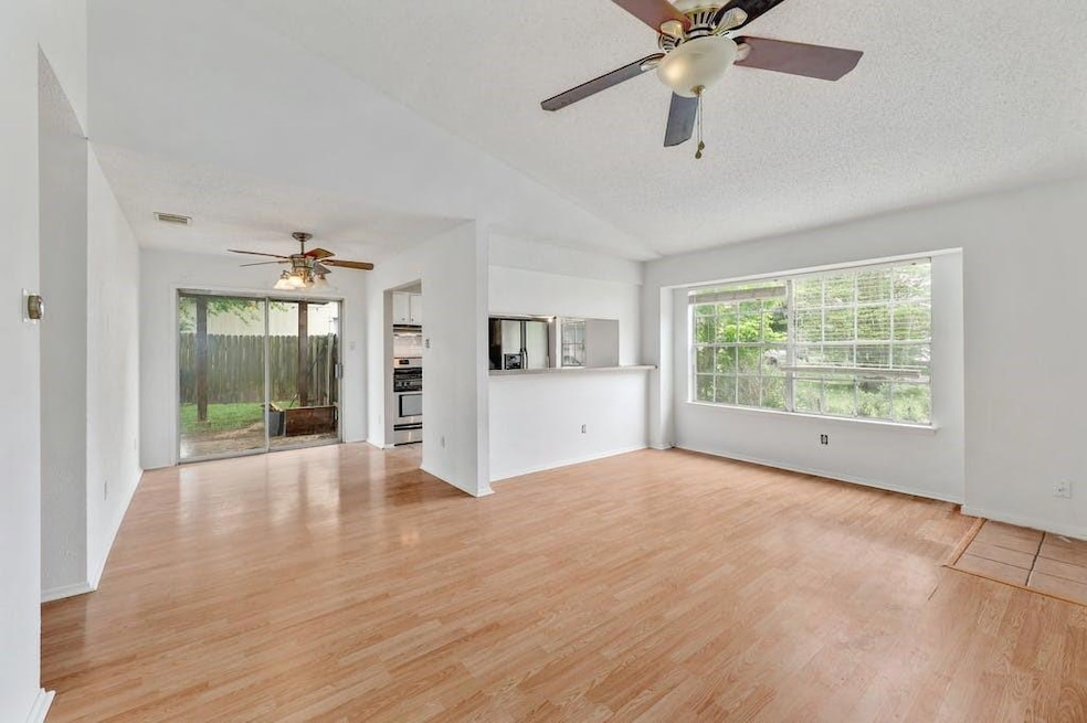 Unfurnished living room with ceiling fan, vaulted ceiling, light wood-type flooring, and a textured ceiling