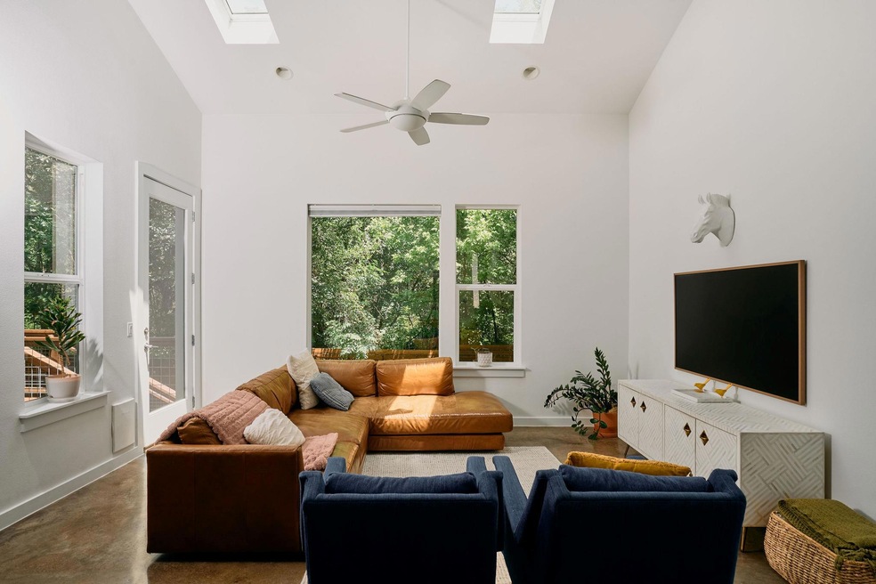 Living room with a skylight, high vaulted ceiling, a ceiling fan, and baseboards