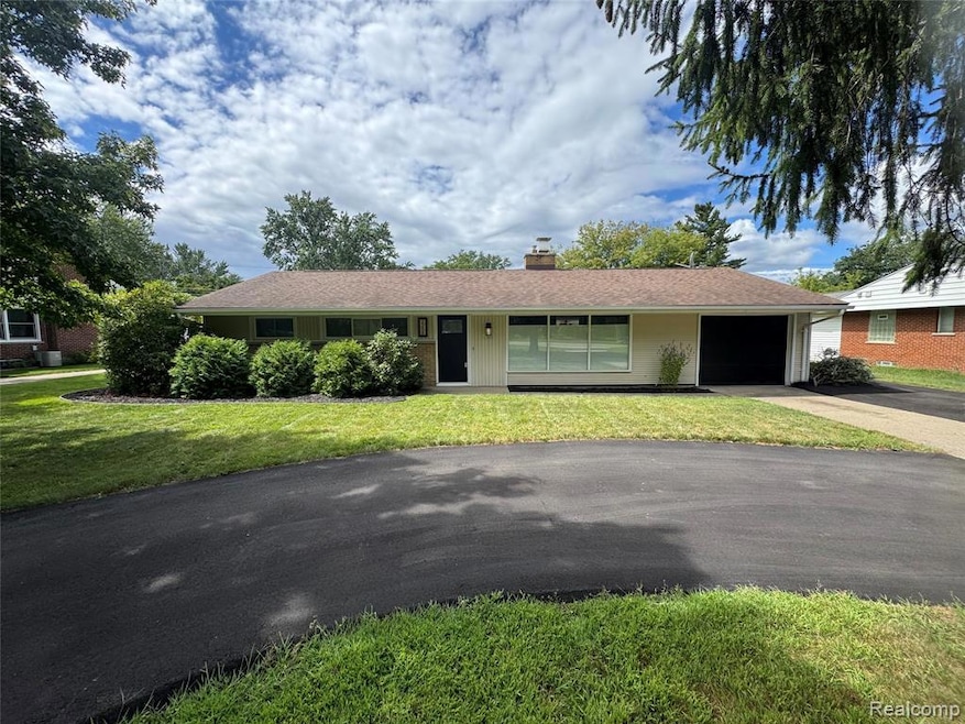 Ranch-style home with an attached garage, driveway, a front lawn, a chimney, and a shingled roof