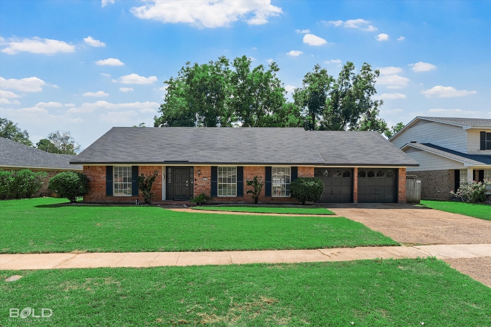View of front of home featuring a front lawn, driveway, brick siding, and roof with shingles