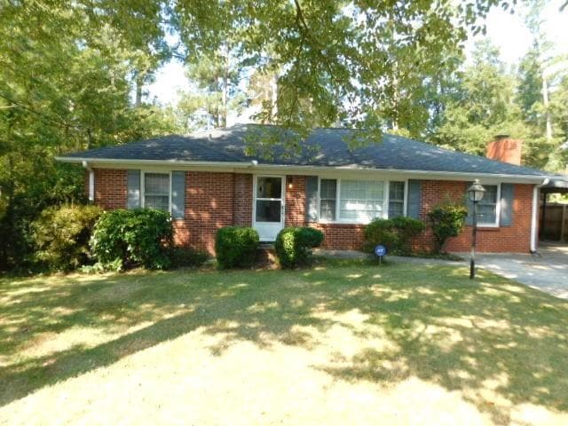 Single story home with brick siding, a chimney, a front yard, and an attached carport