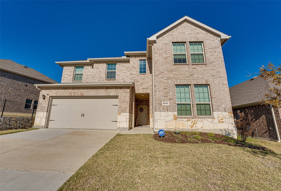 Traditional home featuring driveway, brick siding, a garage, and stone siding
