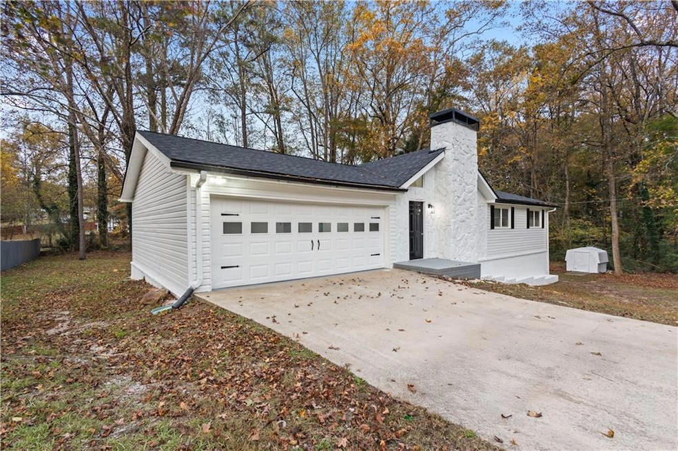View of side of home featuring a garage, driveway, a chimney, and roof with shingles