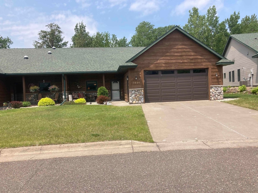 View of front facade with an attached garage, stone siding, concrete driveway, and a front lawn