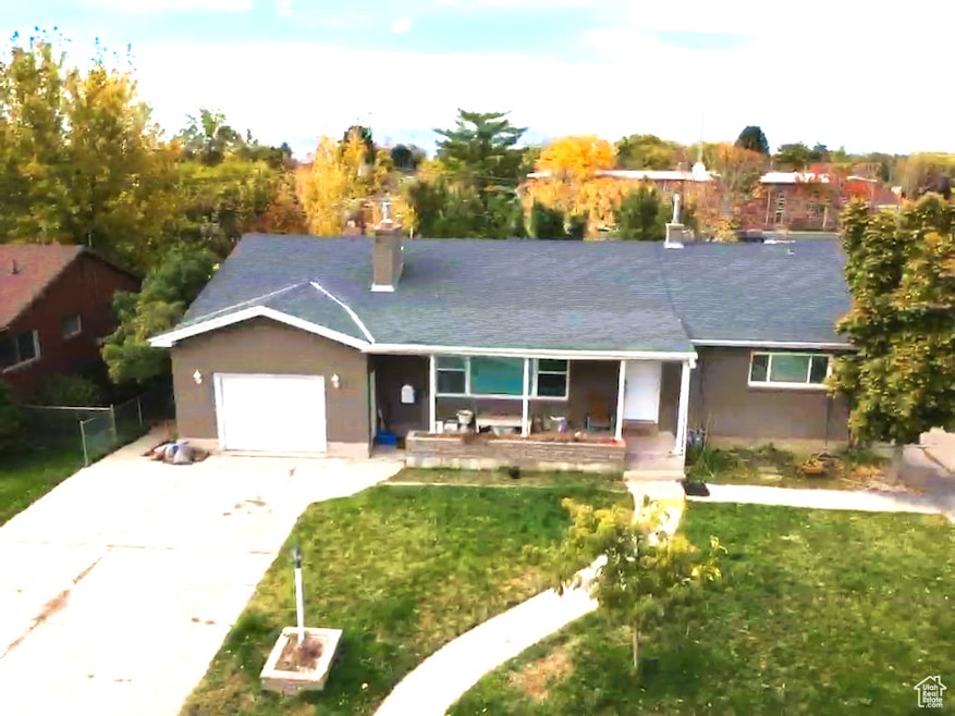 Ranch-style home featuring concrete driveway, covered porch, an attached garage, a front lawn, and a chimney