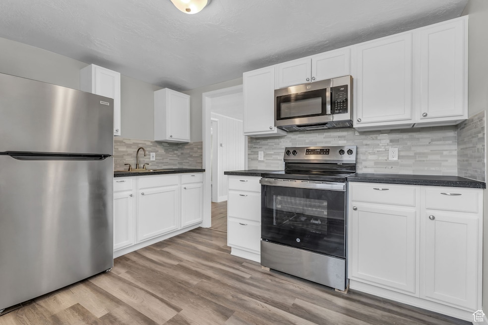 Kitchen with appliances with stainless steel finishes, dark countertops, decorative backsplash, and light wood-style floors