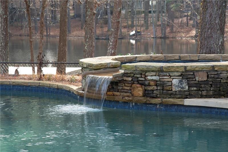 hot tub with water feature into pool, view of pond