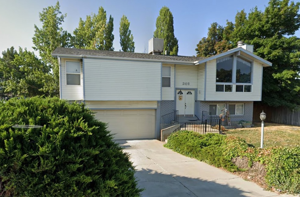 Split foyer home featuring brick siding, a chimney, concrete driveway, an attached garage, and a front lawn
