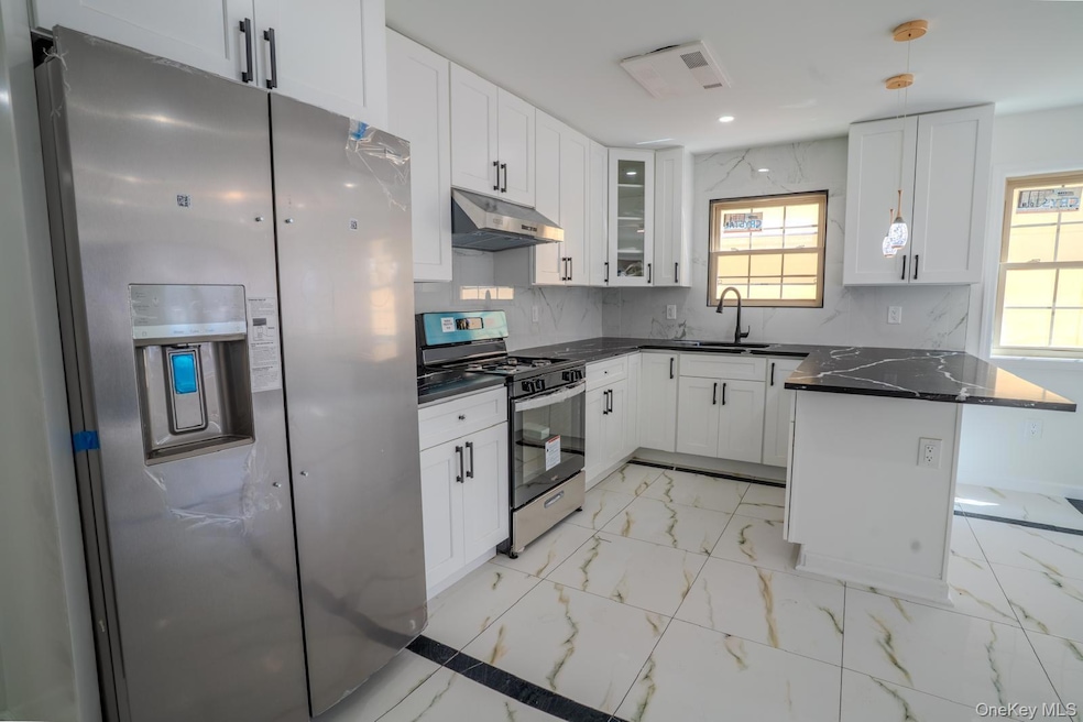 Kitchen with light marble finish flooring, appliances with stainless steel finishes, a peninsula, white cabinetry, and decorative light fixtures