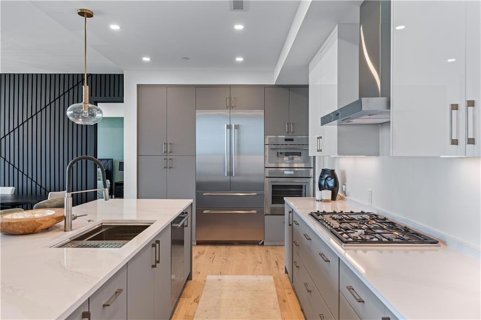 Kitchen featuring gray cabinetry, stainless steel appliances, light wood-style flooring, modern cabinets, and wall chimney exhaust hood