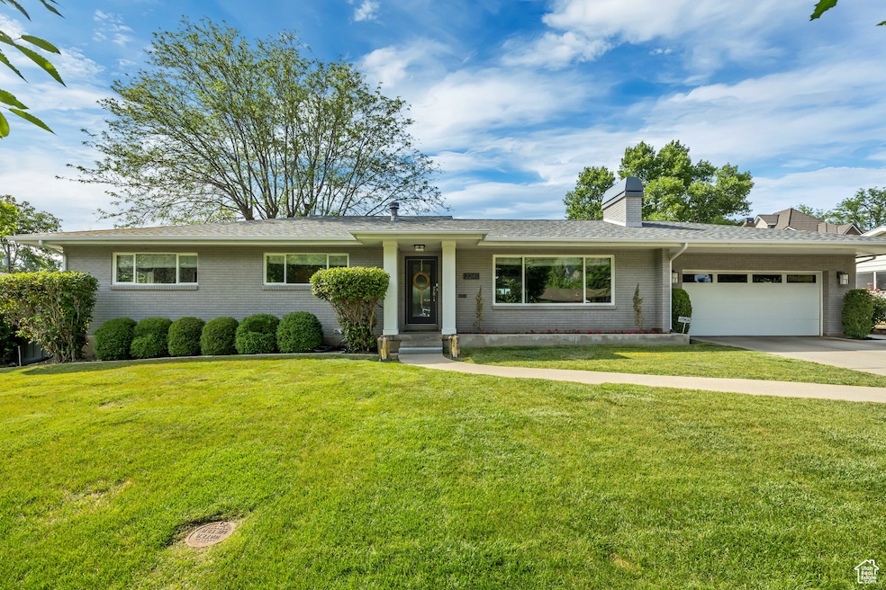 Ranch-style home featuring a garage, brick siding, a chimney, and a front lawn