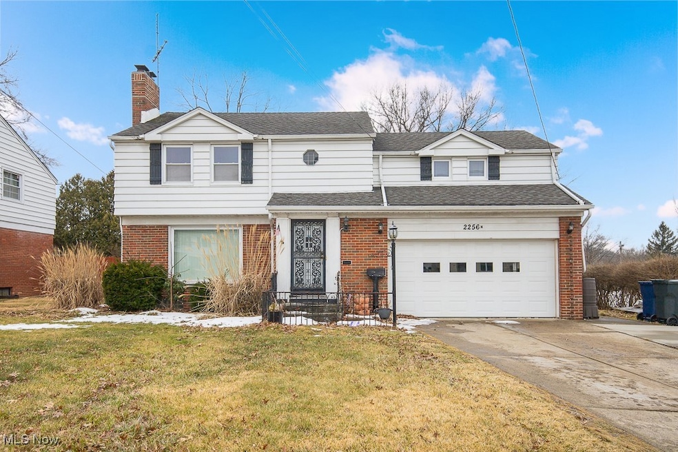 View of front facade with brick siding, concrete driveway, roof with shingles, a front lawn, and a chimney