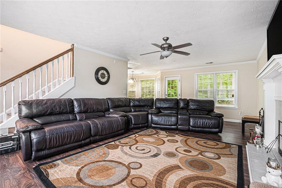 Living area featuring wood finished floors, stairs, ceiling fan, ornamental molding, and a fireplace