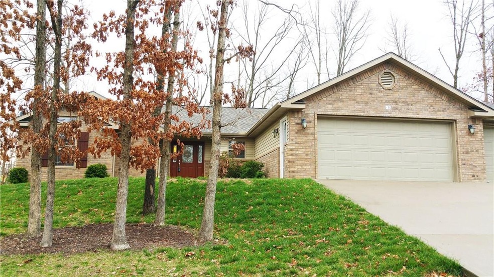 3 car garage brick and vinyl home has a copse of trees in the front.