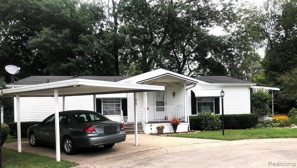 View of front facade featuring a porch, a shingled roof, a front yard, driveway, and view of wooded area