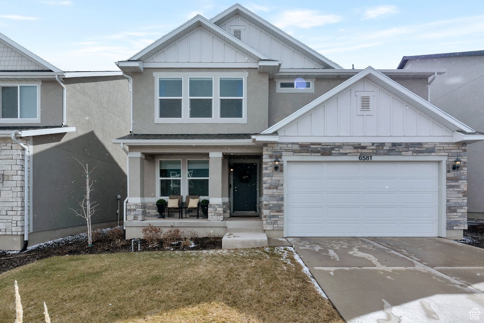 View of front facade featuring board and batten siding, covered porch, driveway, stone siding, and an attached garage