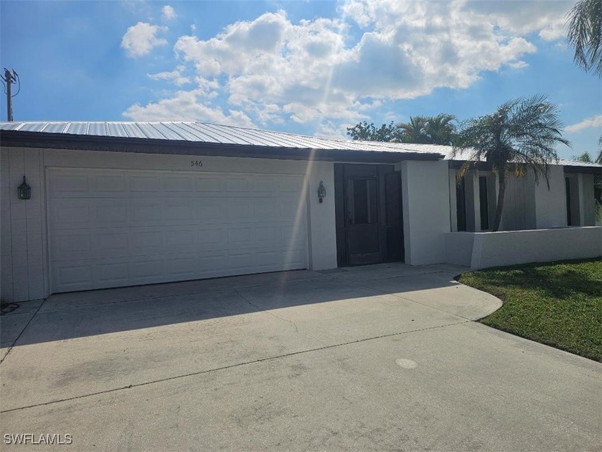 View of front facade with stucco siding, driveway, metal roof, and an attached garage