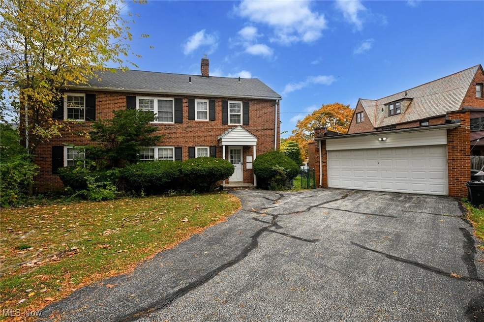 Colonial inspired home with a garage, a chimney, brick siding, a front lawn, and asphalt driveway