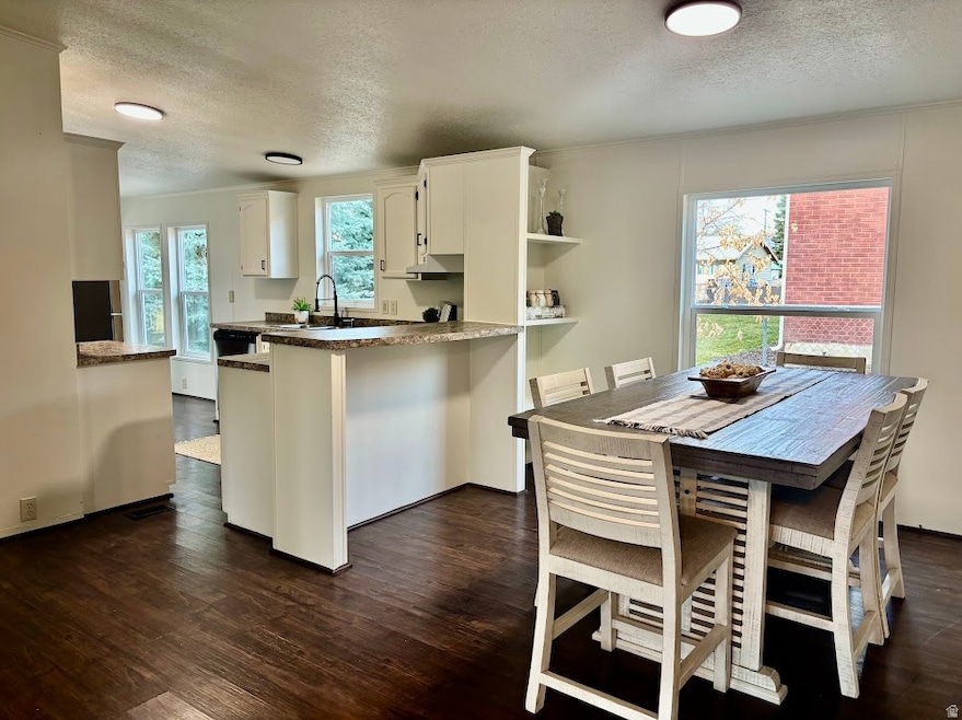 Kitchen featuring a textured ceiling, dark wood-type flooring, crown molding, white cabinetry, and a peninsula