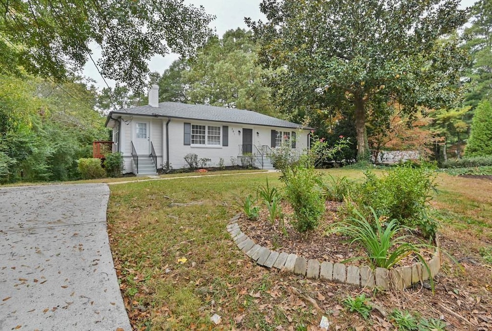 View of front facade featuring a chimney, a front lawn, and view of wooded area