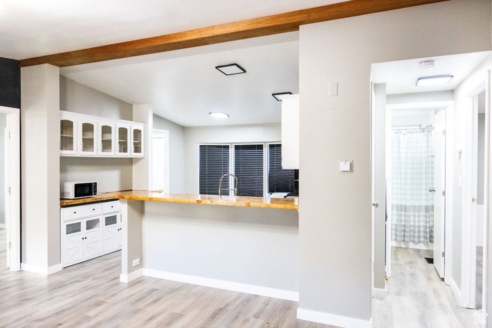 Kitchen with glass insert cabinets, white cabinets, light wood-style flooring, wooden counters, and beamed ceiling