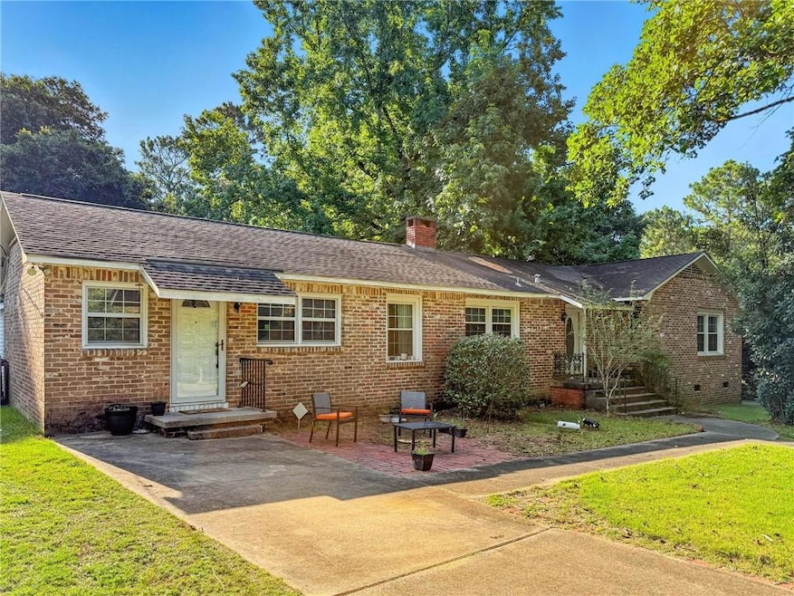 View of front facade with brick siding, a front yard, a chimney, and a shingled roof