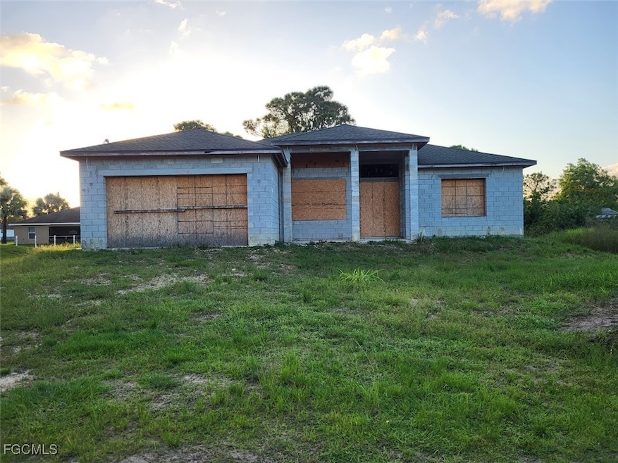 View of front facade featuring a front yard, concrete block siding, and a shingled roof