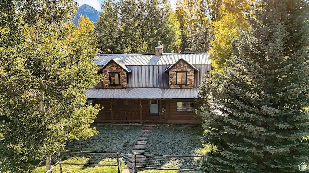 View of front facade with a chimney, a porch, a metal roof, a gate, and a fenced front yard