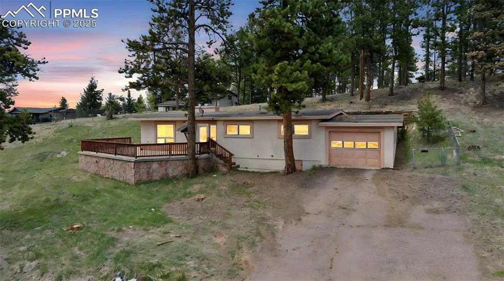 View of front facade featuring stucco siding, a garage, dirt driveway, and a deck