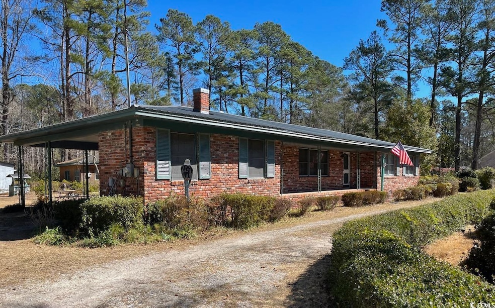 View of home's exterior with dirt driveway, a carport, brick siding, and a chimney