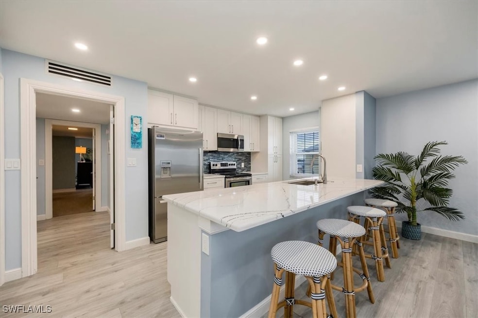 Kitchen with white cabinets, light stone counters, appliances with stainless steel finishes, a breakfast bar, and light wood finished floors