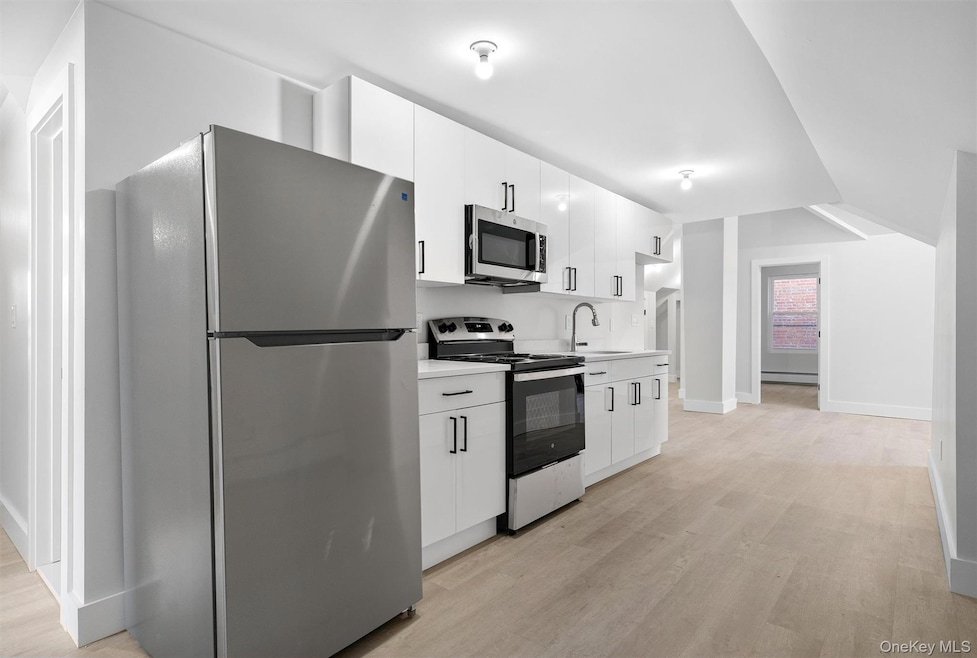 Kitchen with stainless steel appliances, light wood-style floors, light countertops, and white cabinetry