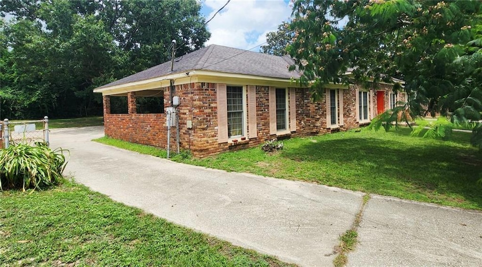View of property exterior featuring a lawn, brick siding, roof with shingles, and driveway