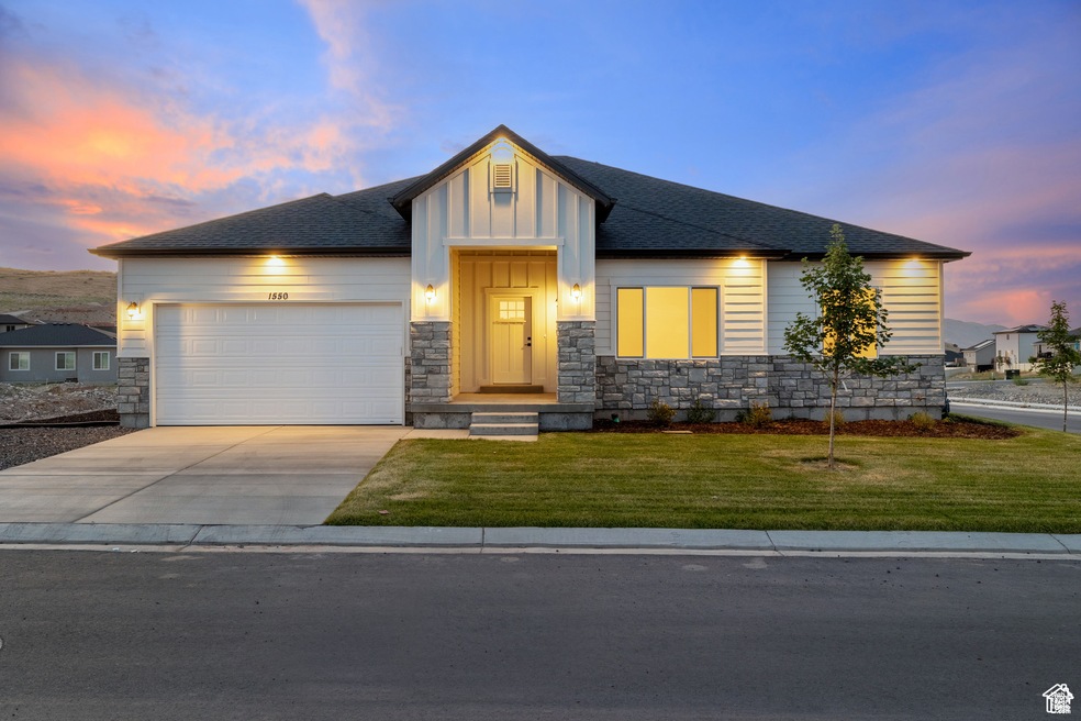 View of front of house with stone siding, an attached garage, concrete driveway, a lawn, and roof with shingles