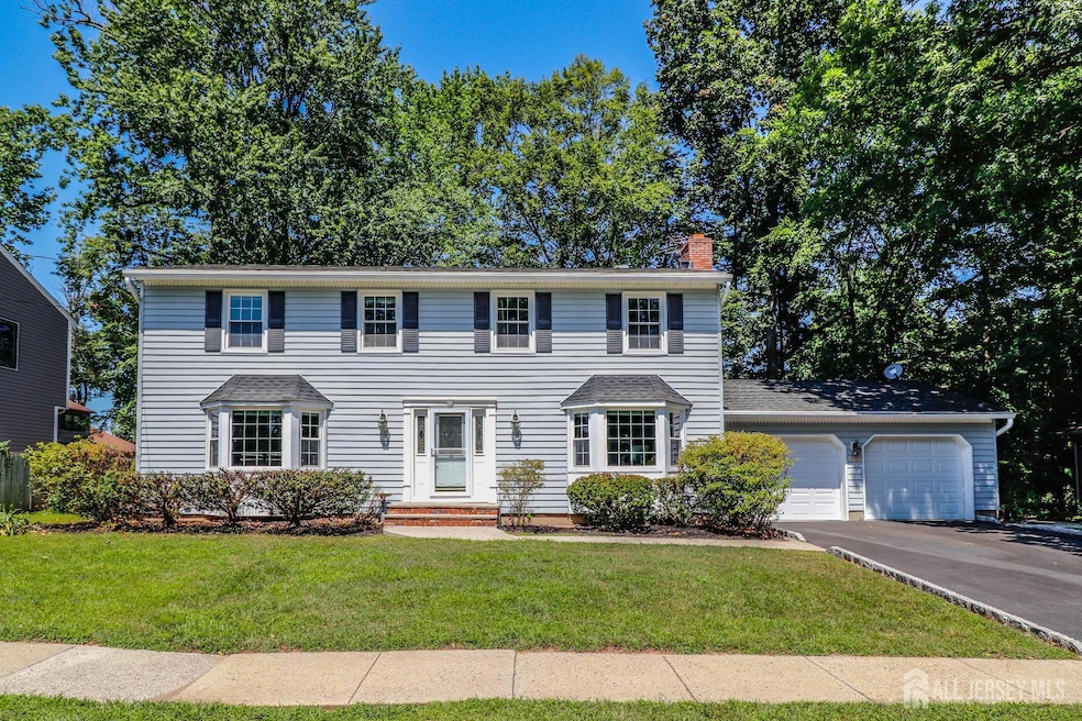 colonial-style house with an attached garage, asphalt driveway, a front yard, and a chimney