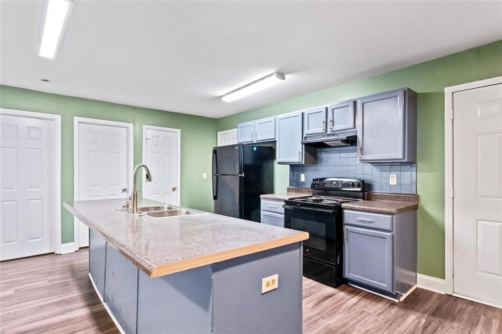 Kitchen with black appliances, tasteful backsplash, an island with sink, and wood finished floors