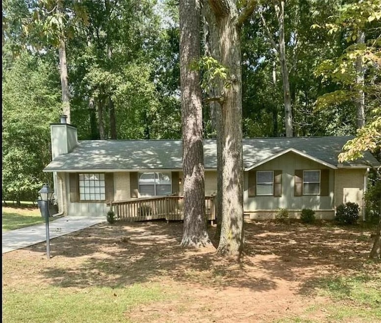Ranch-style home with a chimney, brick siding, and view of wooded area
