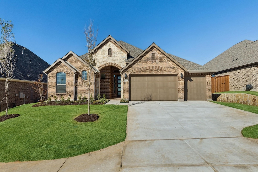 French country inspired facade with brick siding, driveway, a front yard, and an attached garage