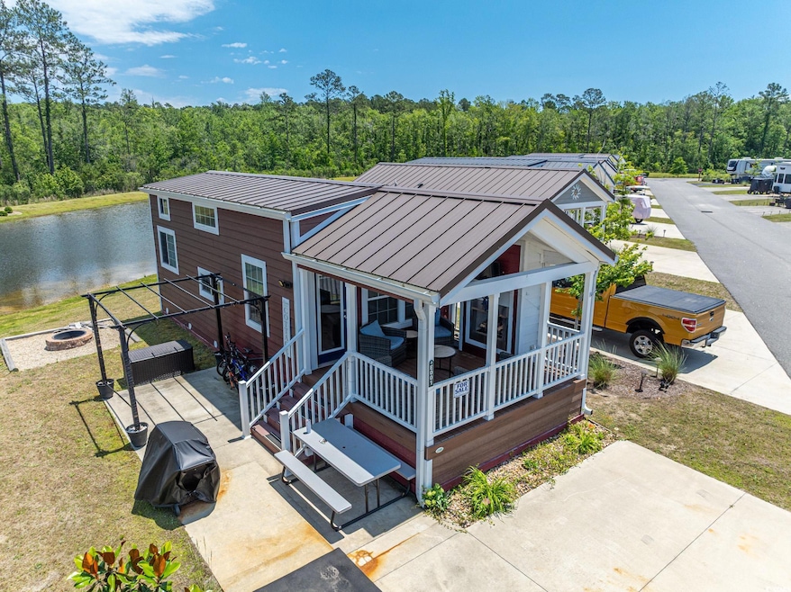 View of front of house featuring a standing seam roof, metal roof, an outdoor fire pit, a water view, and a wooded view