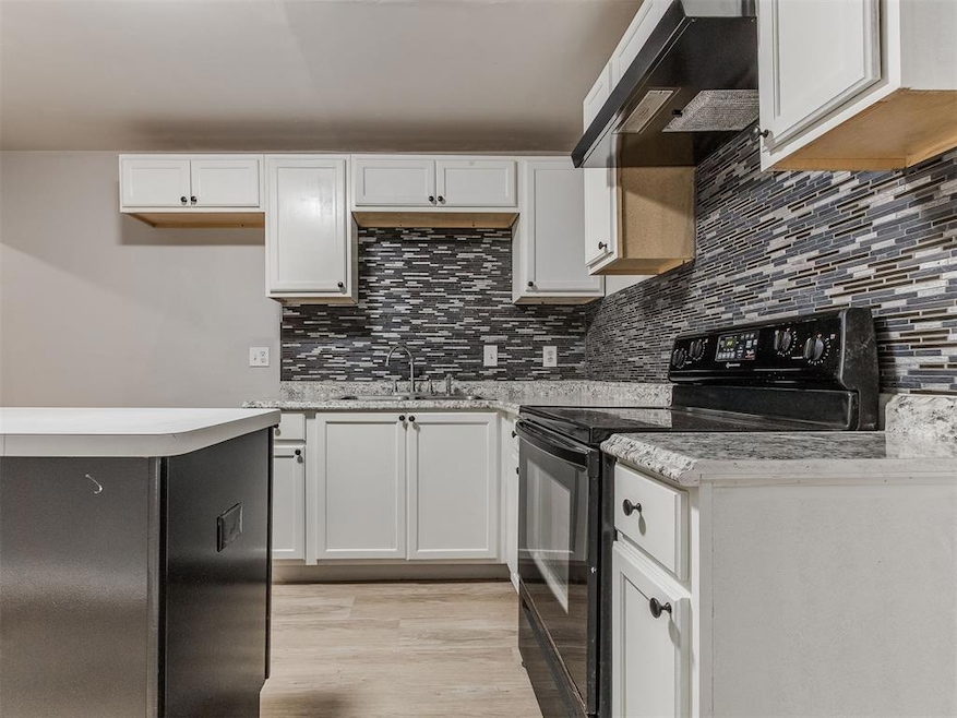 Kitchen with black electric range, backsplash, and white cabinets