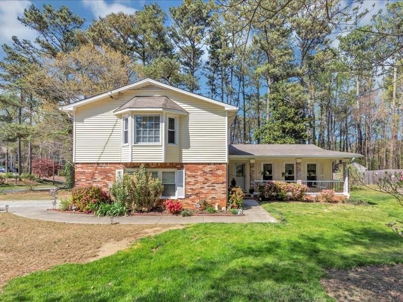 Tri-level home featuring covered porch, brick siding, and a front yard