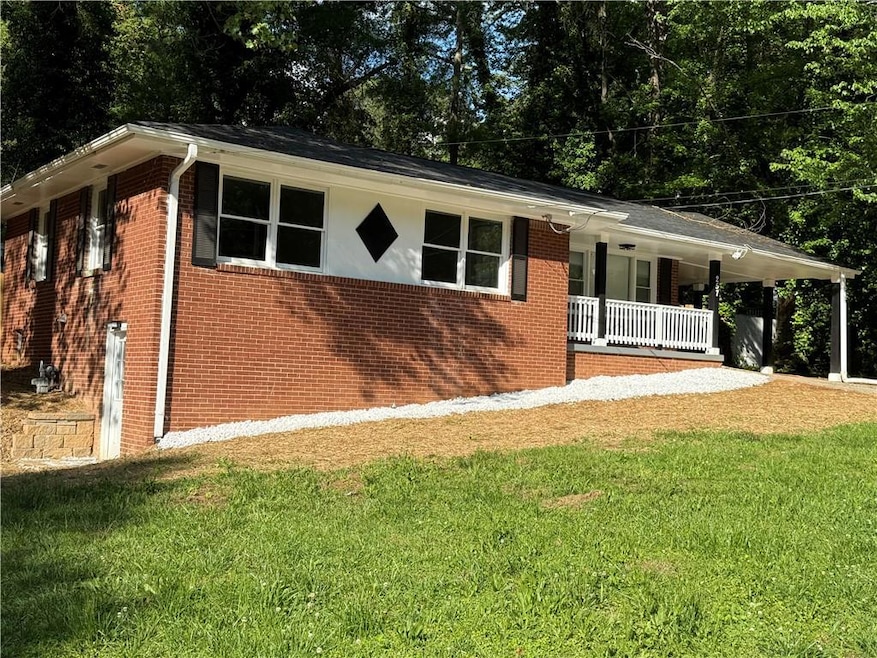 View of side of property with a porch, a lawn, and brick siding