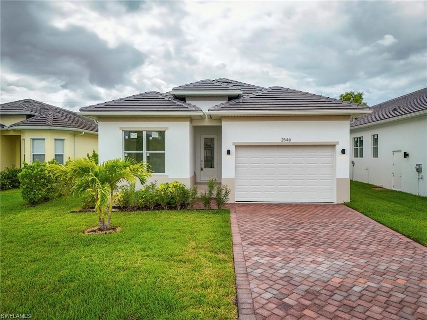 Prairie-style home with decorative driveway, stucco siding, and a front lawn